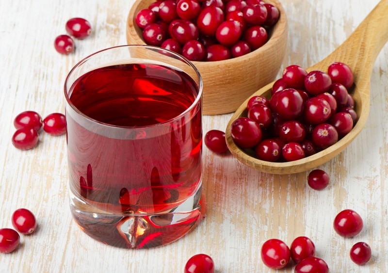 Juice beside cranberries in a wooden spoon