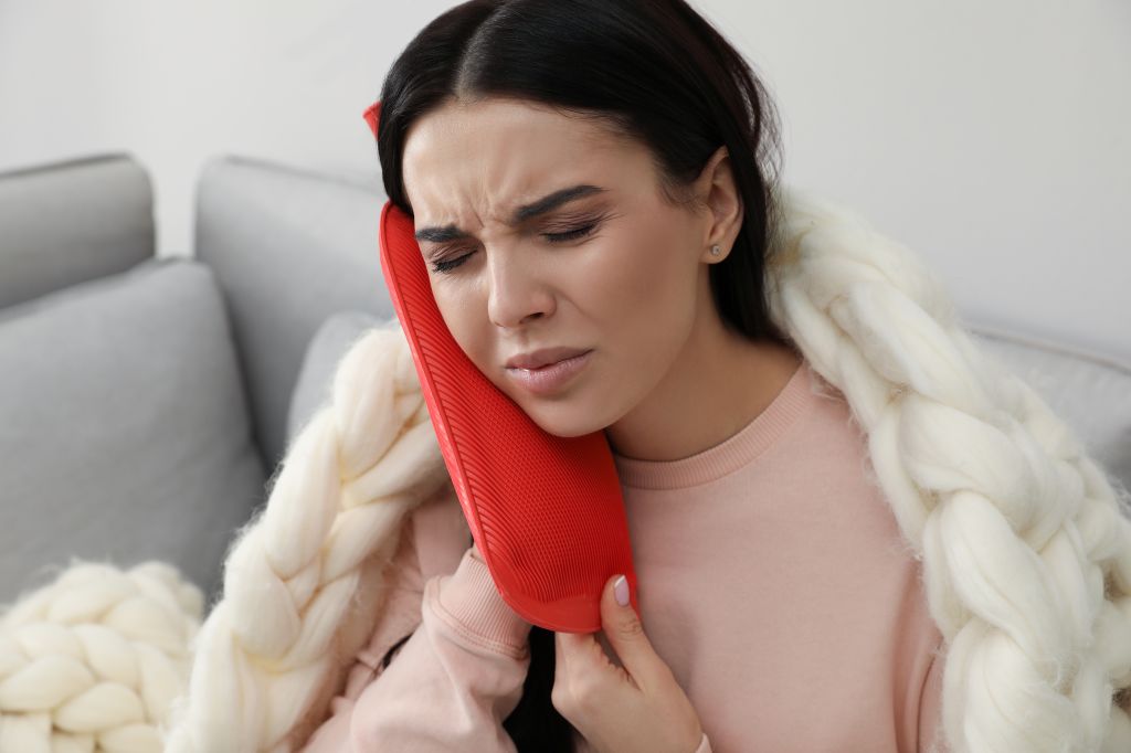 woman using a heat pack on her ear for pain relief ear infection home remedy
