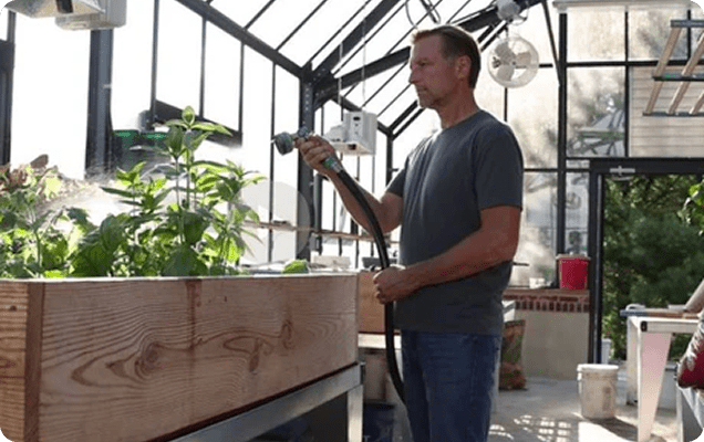 Dr. Berg watering plants in greenhouse.