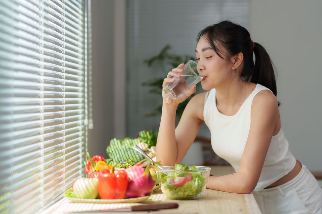 Woman drinking water next to a bowl of salad 