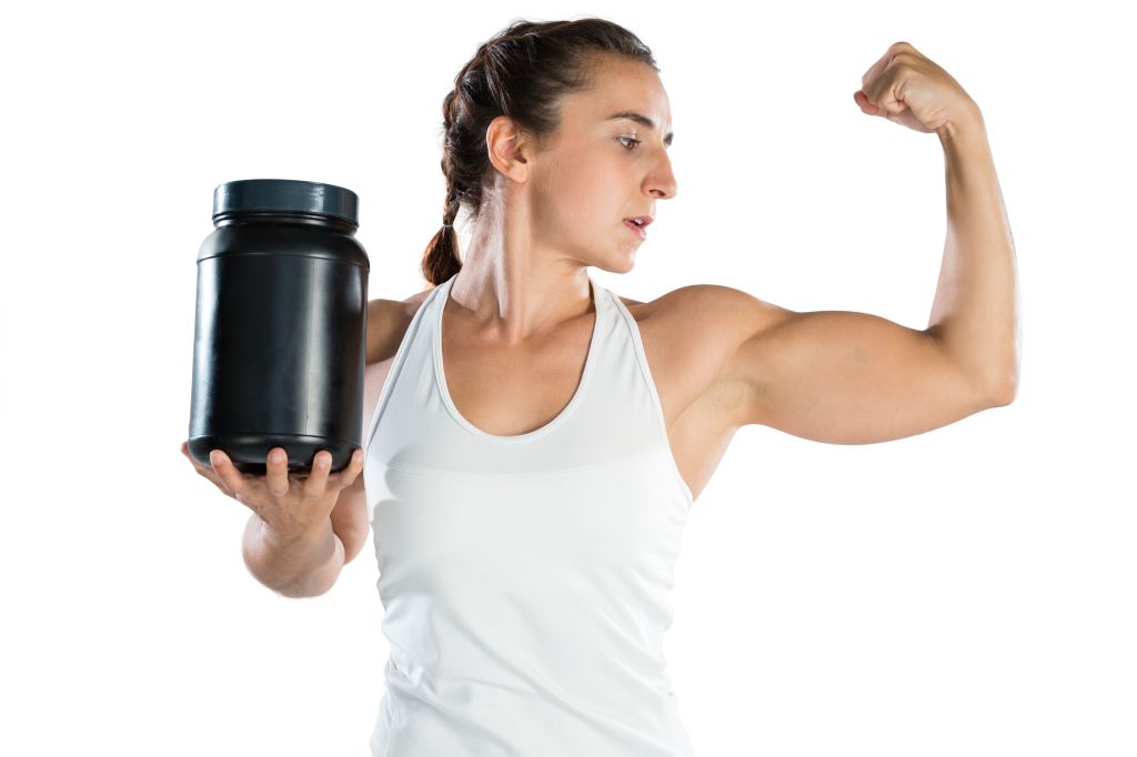 Woman flexing muscles while holding a supplement bottle