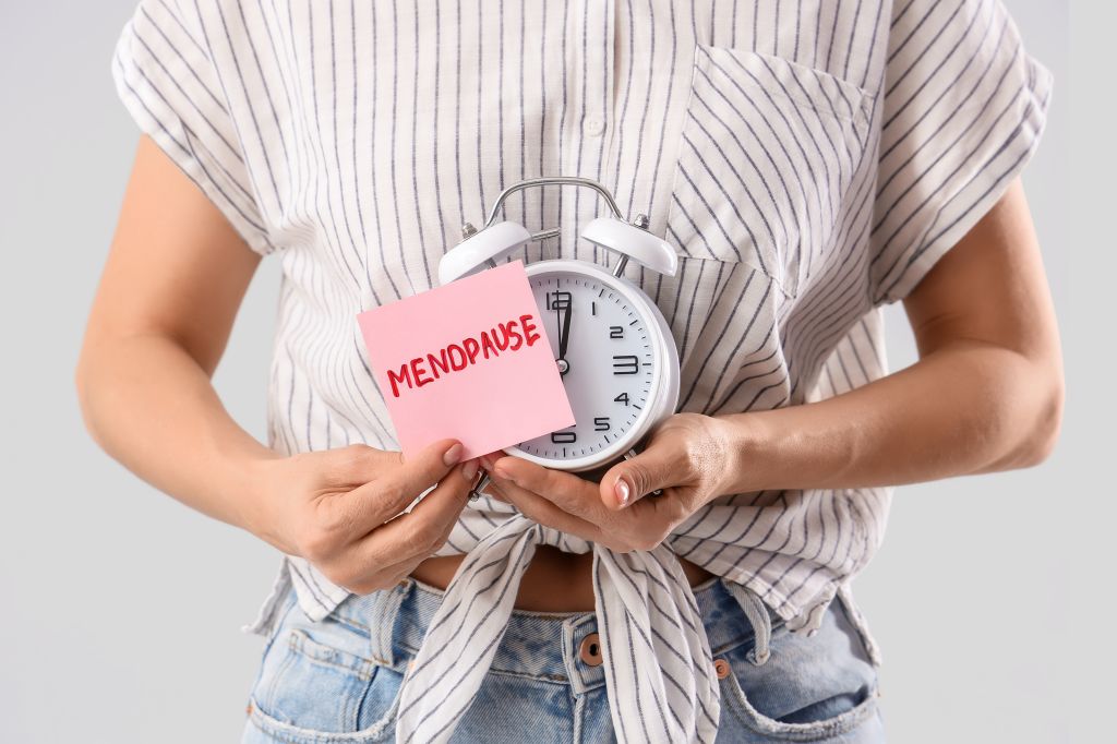 Woman holding paper with the word “menopause” and an alarm clock